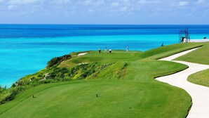 Campo de golf con vista despejada al océano y una construcción distante.