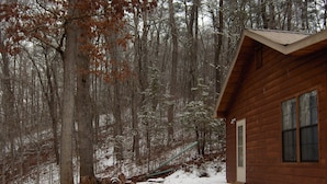 Una cabaña de madera con techo inclinado, rodeada de un bosque cubierto de nieve.