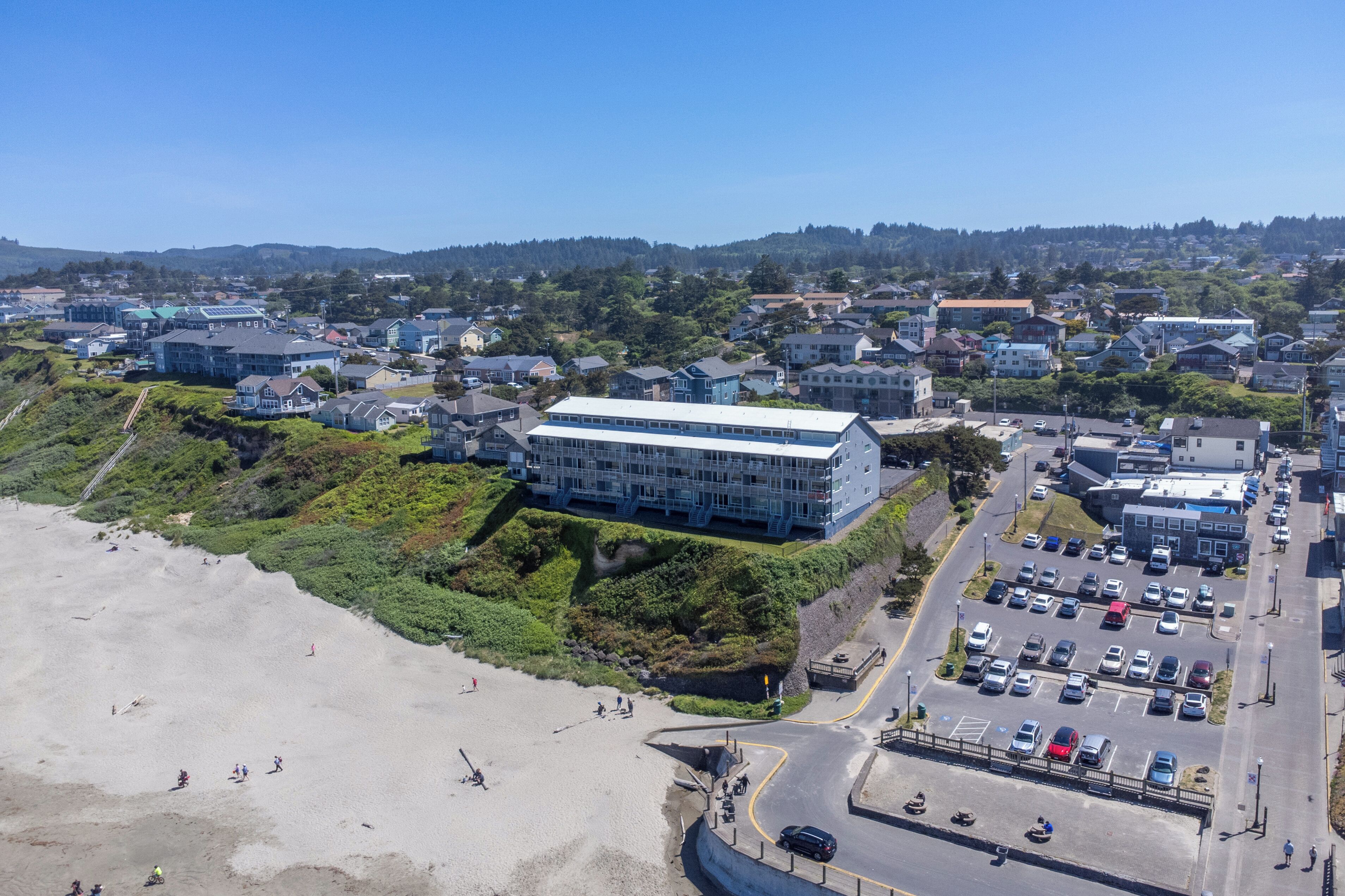 An aerial view of a coastal town with a prominent building, a parking lot, and a beach.