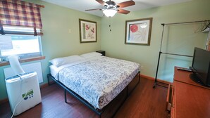 Un dormitorio con cama, ventilador de techo, calefactor, televisor y fotografías enmarcadas en la pared.