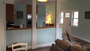 Una cocina con armarios de madera, un refrigerador y un microondas. Hay una mesa de comedor con sillas y un sofá en la sala.