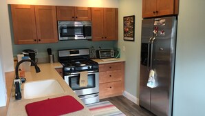 Cocina compacta con armarios de madera, refrigerador de acero inoxidable, microondas, estufa y pileta.