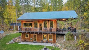 A two-story log cabin with a balcony, surrounded by a forest.