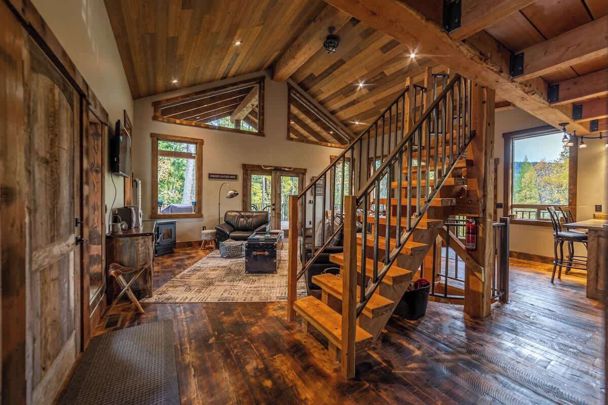 A spacious living area with a wooden staircase, large windows, and a cozy fireplace.