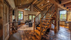 A spacious living area with a wooden staircase, large windows, and a cozy fireplace.