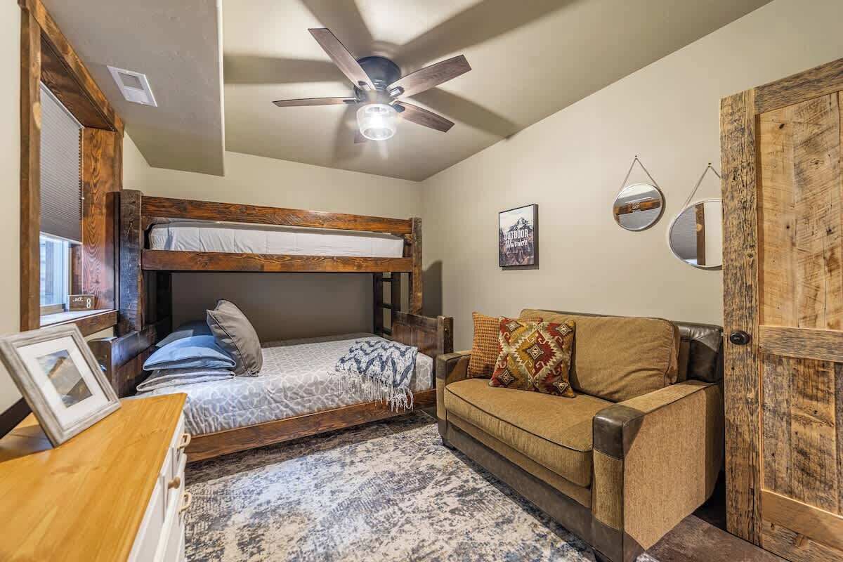 Habitación pequeña con una cama individual alta, un sofá, un ventilador de techo y una puerta de diseño rústico.