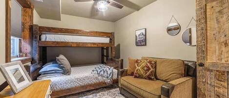 Habitación pequeña con una cama individual alta, un sofá, un ventilador de techo y una puerta de diseño rústico.
