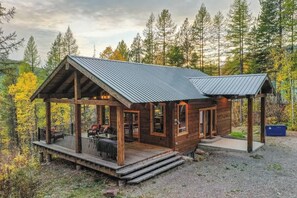 Eine Holzhütte mit einem Metalldach, einer Veranda mit Sitzgelegenheiten und einem Schotterweg.