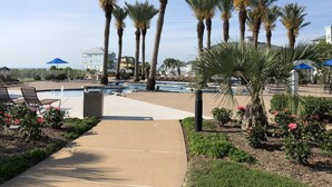 A pool area with lounge chairs, palm trees, and a clear sky. - BEACH FRONT!  The Happy Mullet: Surf, Sun, the Perfect House and Ms. Pac Man (Galveston)