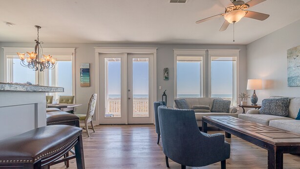 A spacious living room with a large window, a ceiling fan, and a dining area with a bar stool. - BEACH FRONT!  The Happy Mullet: Surf, Sun, the Perfect House and Ms. Pac Man (Galveston)