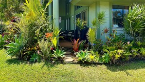Une maison dotée d’un porche abrité, entourée d’une végétation tropicale luxuriante et d’une pelouse bien entretenue.