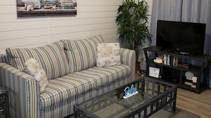 A living room with a striped sofa, a glass coffee table, a television, and a plant. - Paradise found -  close to everything and endless beautiful beach access (FT Walton beach)