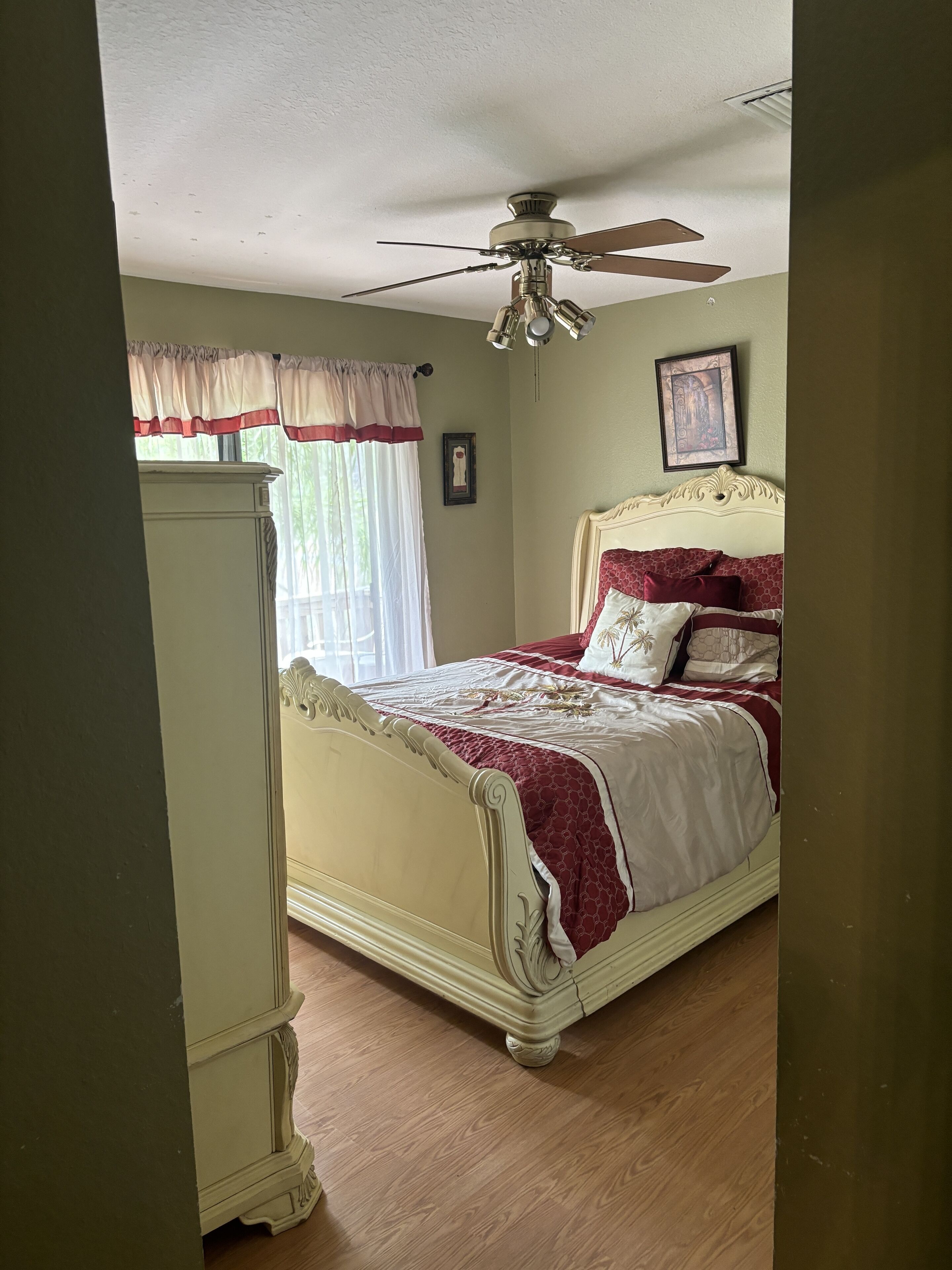 A bedroom with a bed, a ceiling fan, a window with curtains, and a framed picture on the wall.