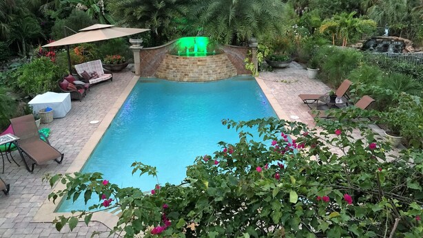 Une piscine agrémentée d’une cascade, entourée d’une végétation luxuriante et dotée d’un espace salon extérieur.