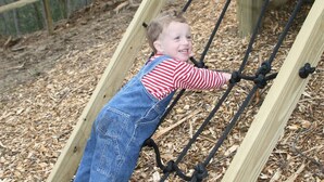 A child climbing a wooden structure with ropes.