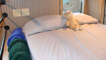 Una cama con un oso de peluche, una manta verde enrollada y una manta azul.