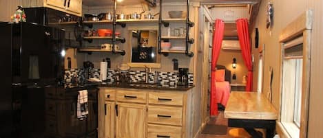 Una cocina compacta con armarios de madera, un refrigerador negro y un comedor con mesa y sillas.
