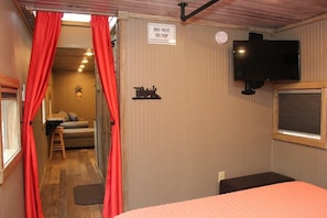 A room with a bed, a television, a sign that says 'DO NOT HUMP,' and a small table with a chair.