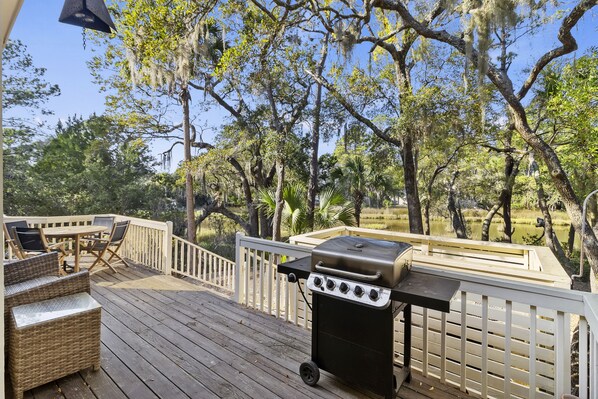A wooden deck with a grill and seating area, surrounded by trees and a fence.