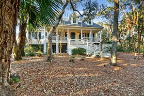 A large house with a covered porch, a staircase, and a well-maintained yard with trees and mulch.