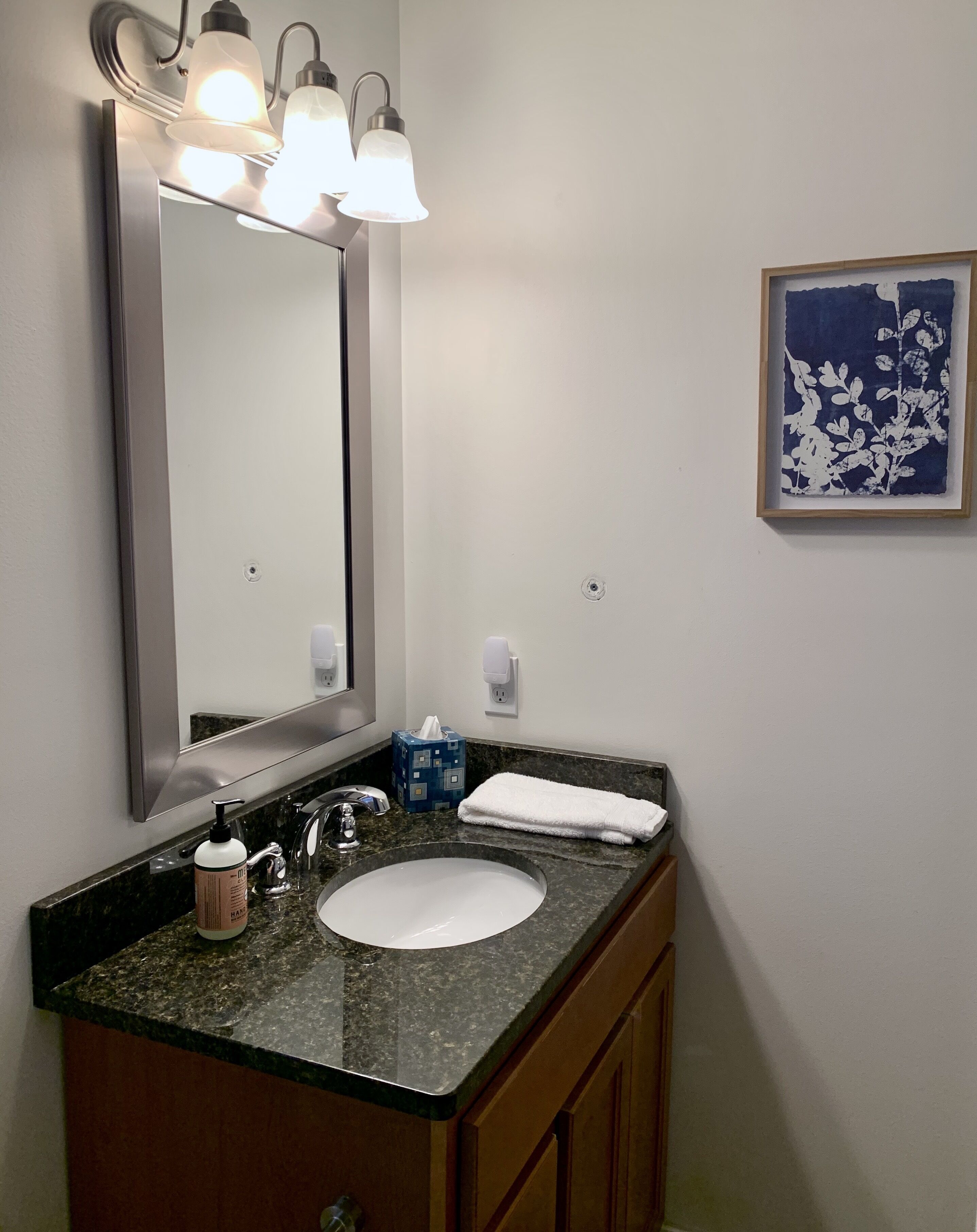 A bathroom with a large mirror, a sink, a towel, and a framed picture on the wall.