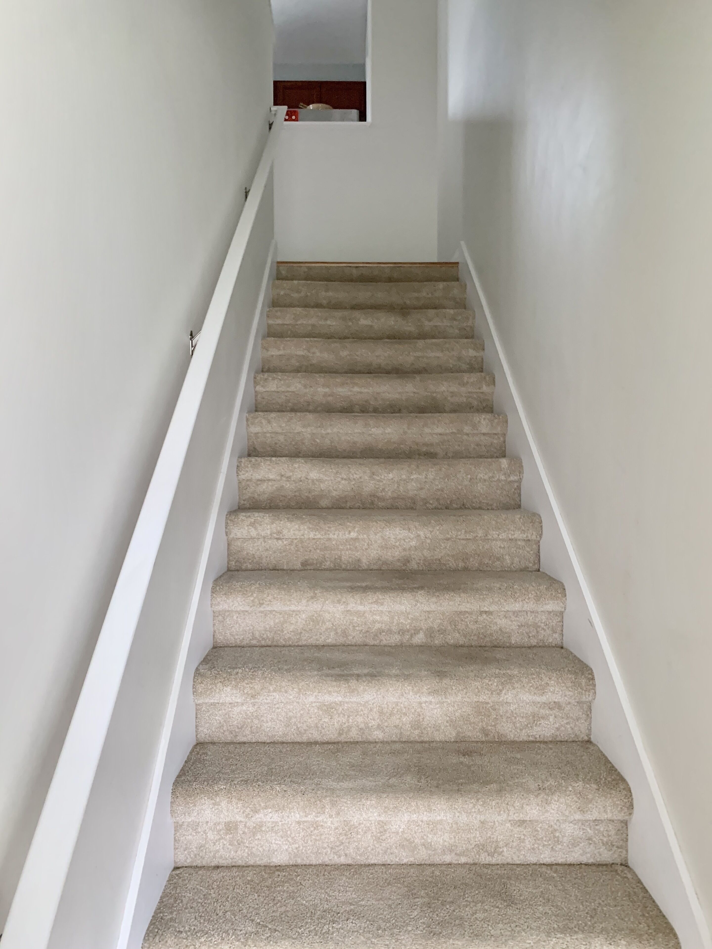 Una escalera alfombrada con paredes blancas y un pequeño ventanal en la parte superior.
