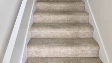 Una escalera alfombrada con paredes blancas y un pequeño ventanal en la parte superior.