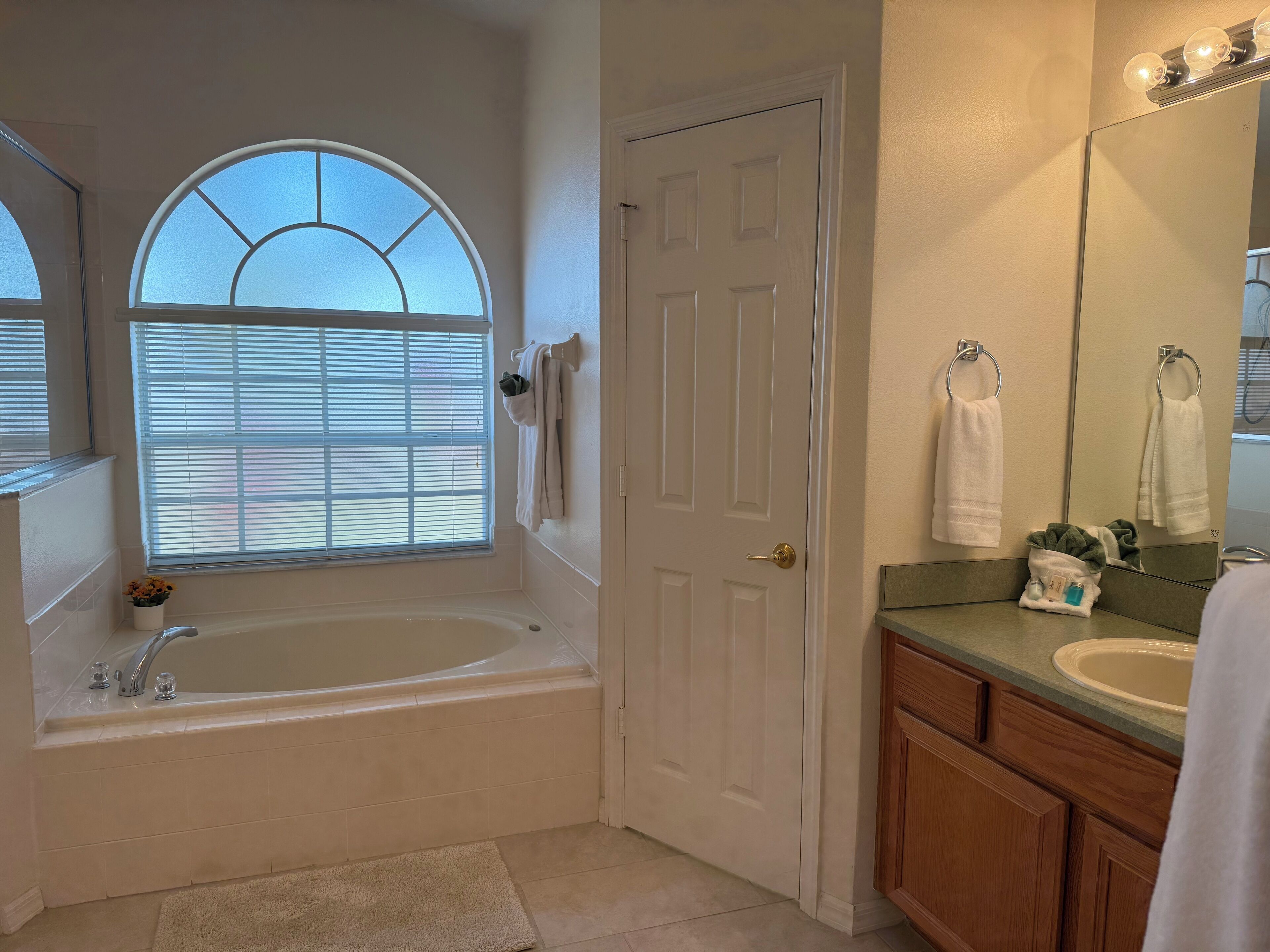 A bathroom with a freestanding bathtub, a vanity with a sink, a mirror, and a door with a towel rack.