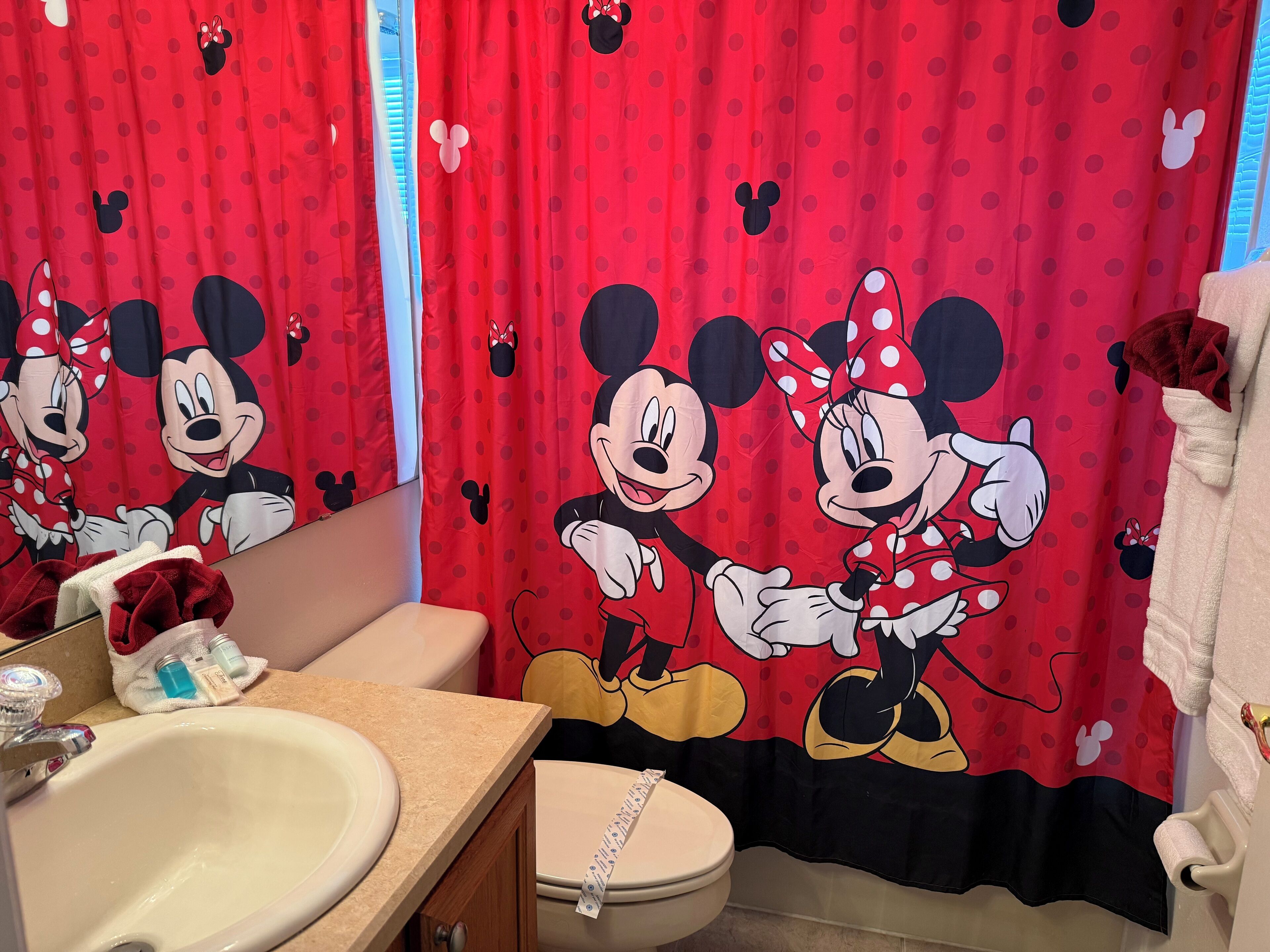 Ein Badezimmer mit Duschvorhang im Mickey-Mouse-Design, einem Waschbecken und einer Toilette.