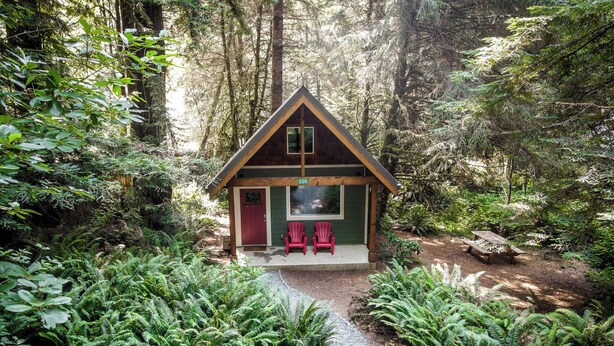 Une cabane avec une véranda, deux chaises Adirondack rouges et un chemin de gravier menant à l’entrée.