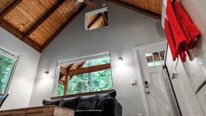 Une pièce avec un plafond en pente, des poutres en bois, un ventilateur de plafond, une fenêtre donnant sur des arbres, une porte blanche et une serviette rouge accrochée à une armoire blanche.