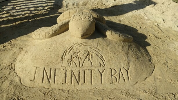Hiekasta veistetty rapuaiheinen hiekkaveistos, jonka hiekkaan on kaiverrettu sanat »INFINITY BAY».
