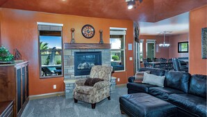 A living room with a fireplace, a black leather sofa, and a patterned armchair. - 5 Bedrooms with Heated Private Pool, Last minute rates are posted! (Saint George/Washington)