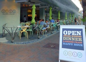 Un espacio de comedor al aire libre con mesas y sillas, un letrero que anuncia una cena galardonada y el nombre del restaurante en la pared.