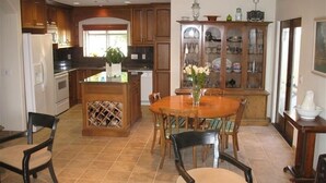 A kitchen with wooden cabinets, a central island with a wine rack, a dining table with chairs, and a glass-fronted cabinet with dishes. - 4 Bedroom plus den/office 3 Bath Private House W/Pool & Hot Tub in Palm Spring (Palm Springs)