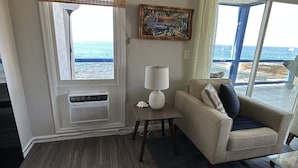 Habitación con un ventanal que ofrece vistas al mar, un sofá color beige con cojines, una mesita con una lámpara y un aire acondicionado instalado en la pared.