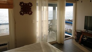 Un dormitorio con cama, televisor, ventana con cortinas, un adorno en la pared y vista al mar.