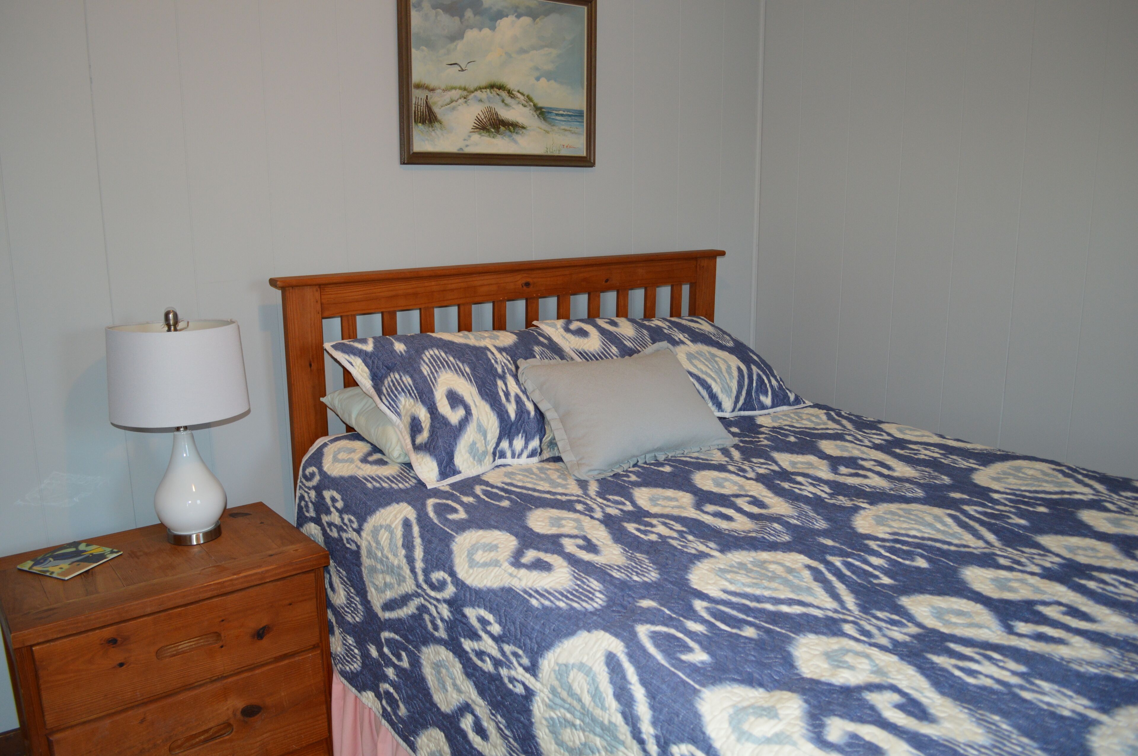 A bedroom with a wooden bed, a nightstand with a lamp, and a painting on the wall.
