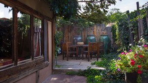 A patio area with a table and chairs, surrounded by a wooden fence and potted plants.