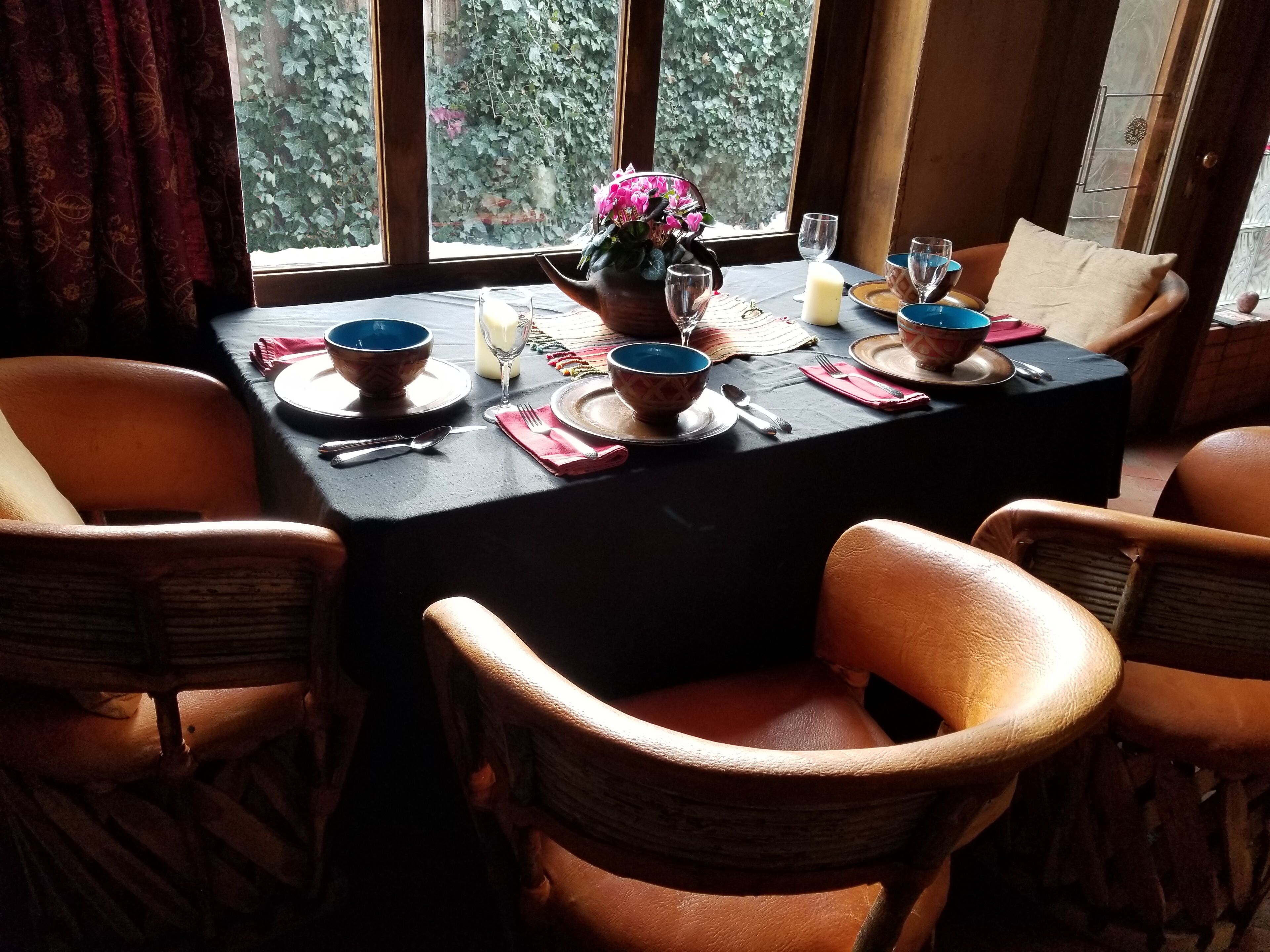 Een eettafel gedekt met blauwe en beige kommen, borden en bestek, met een bloevas en een kaars op tafel.