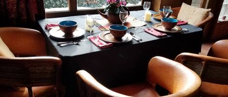 Een eettafel gedekt met blauwe en beige kommen, borden en bestek, met een bloevas en een kaars op tafel.