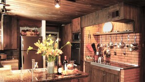 A kitchen with wooden cabinets, a granite countertop, a hanging pot rack, and a vase with flowers.