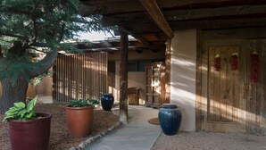 A covered outdoor area with a wooden door, large potted plants, and a stone pathway.