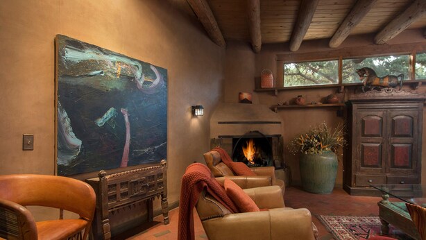 A cozy living room with a fireplace, leather armchairs, a large abstract painting, and rustic decor.