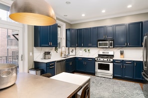 A modern kitchen with dark blue cabinets, stainless steel appliances, and a large hanging light fixture.