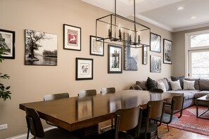 A dining area with a long table and chairs, a chandelier, and framed pictures on the wall.