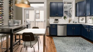 Una cocina moderna con gabinetes azul oscuro, lavavajillas de acero inoxidable y un comedor con mesa y sillas blancas.