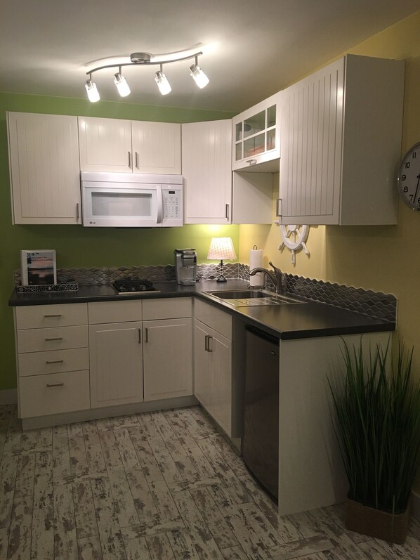 A kitchen with white cabinets, a microwave, a coffee maker, and a clock on the wall.