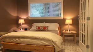 A bedroom with a wooden bed, two bedside tables with lamps, a window with blinds, and a door with glass panels. - the Beach Suite on Lemolo!    CLEAN & PRIVATE ... getaway & relax. (Poulsbo)