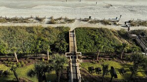 A beach with a wooden boardwalk leading to a grassy area with palm trees and benches. - Oceanfront Gem Clean 1080sf New Furniture, Beds, Carpet Free WiFi Cable Gym Park (Myrtle Beach)